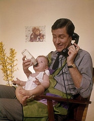 Father on phone feeding baby from Flickr "The Commons" to illustrate How to set up a major gift solicitation appointment